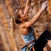 Woman in climbing gear climbing up cliff